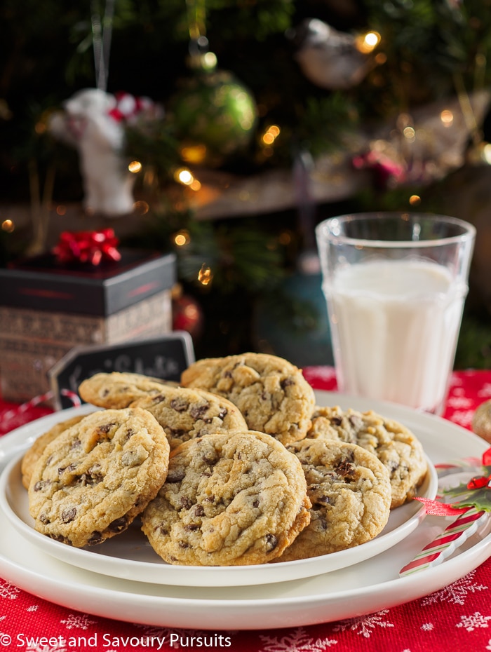 Chewy chocolate chip cookies on white dish with glass of milk.