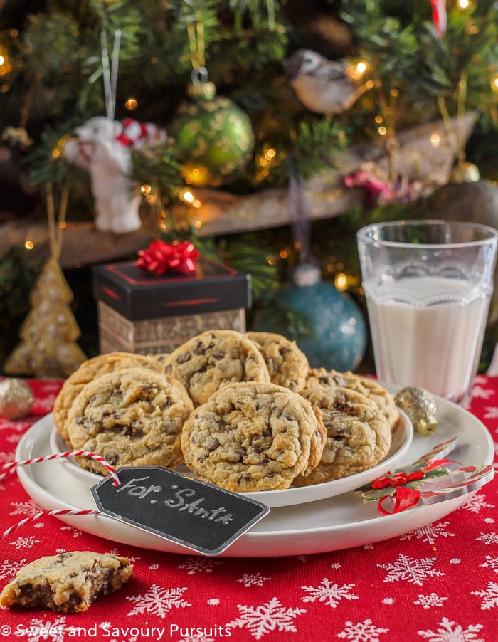 Chewy chocolate chip cookies on dish with glass of milk for Santa.