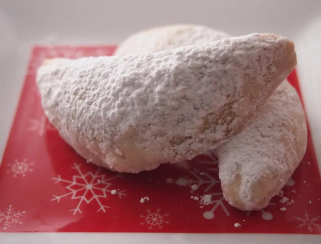Crescent shaped Christmas cookies rolled in confectioners' sugar on a red and white plate.