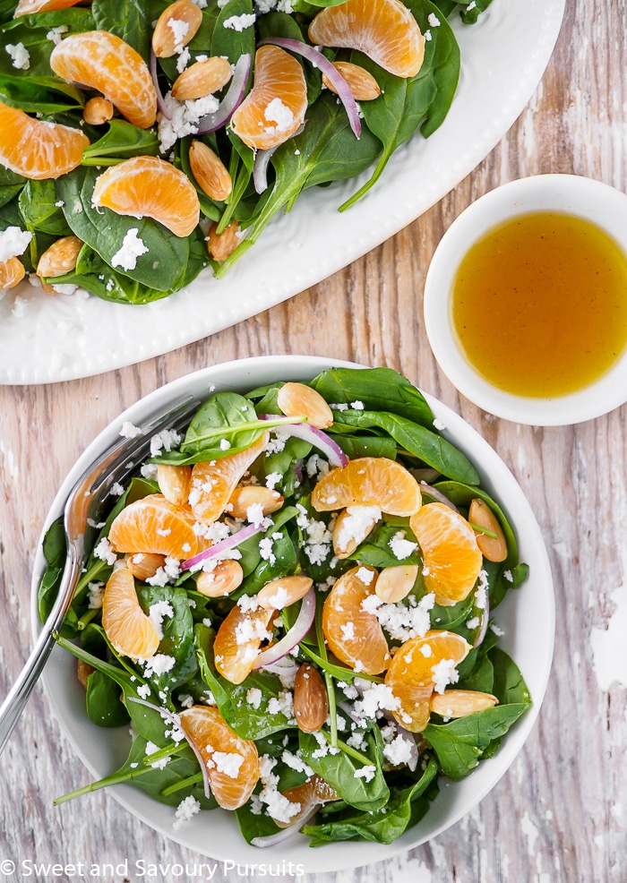 Top view of Spinach and Clementine Salad served in bowl with extra dressing on the side.