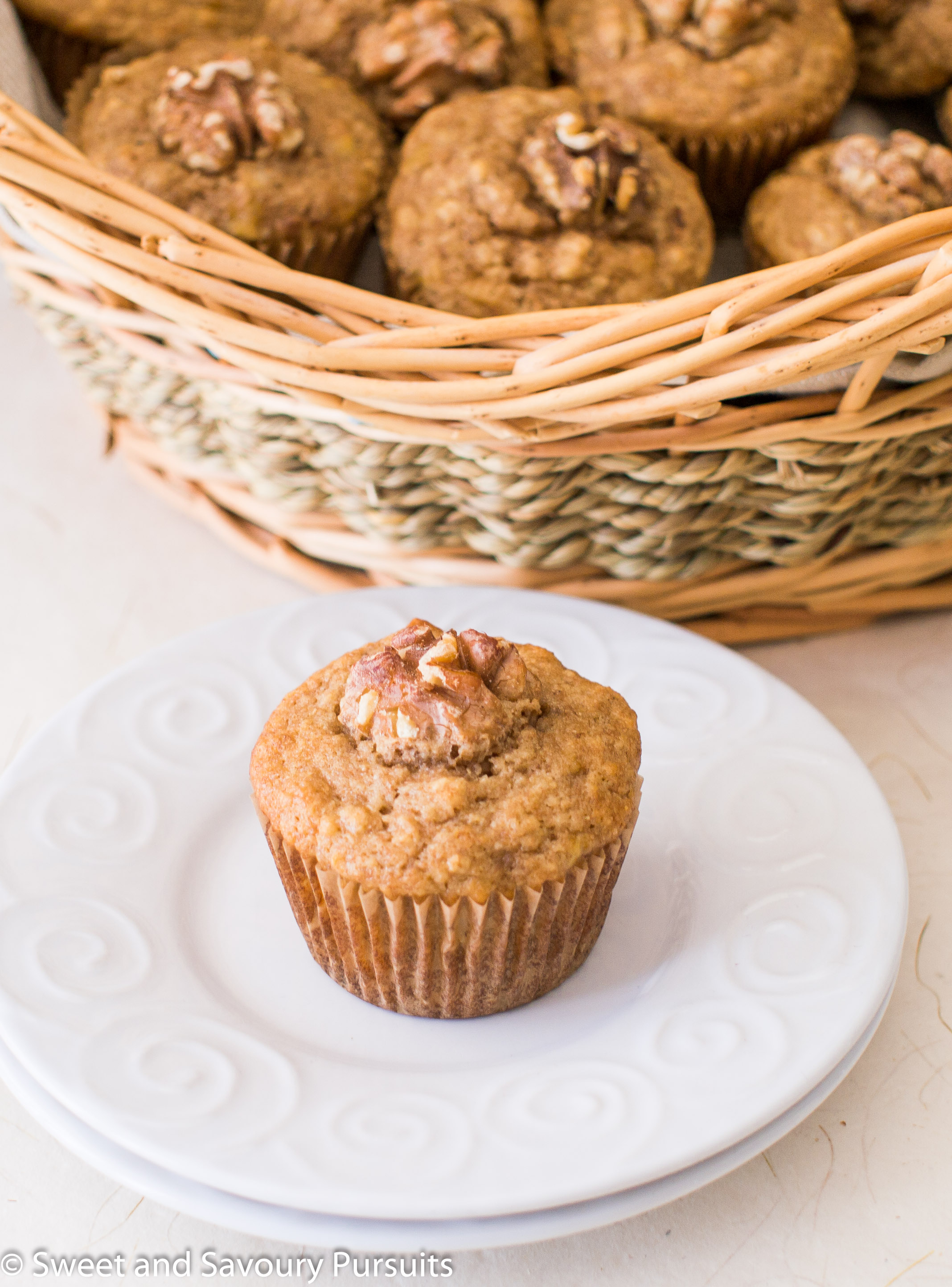 Banana nut muffin on small dish with basket of muffins in the background.