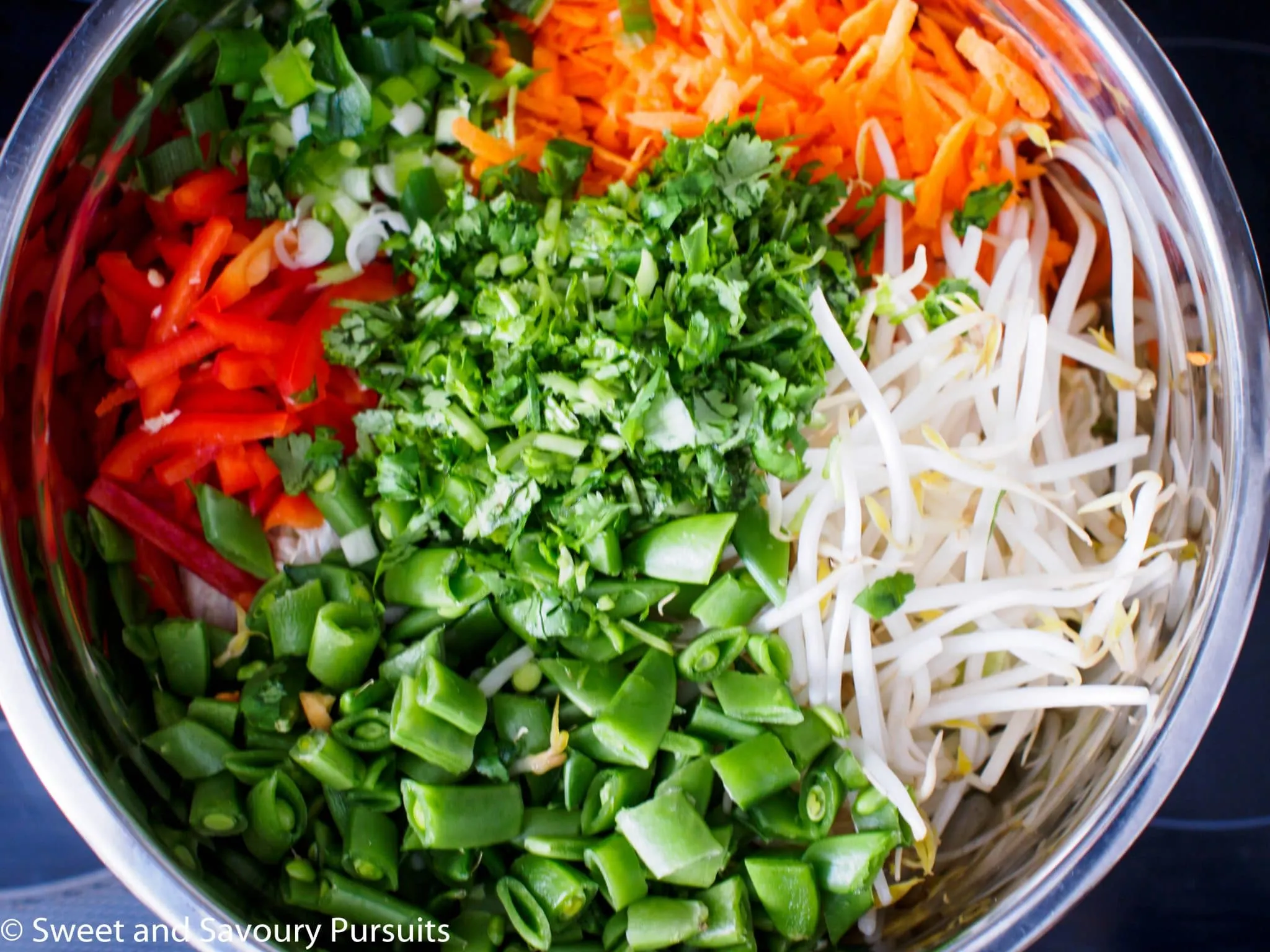 Large bowl with shredded carrots, red pepper, sugar snap peas, bean sprouts and chopped cilantro for an Asian-style salad.