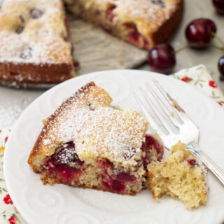 Slice of Cherry Almond Cake with a dusting of powdered sugar on white dish.