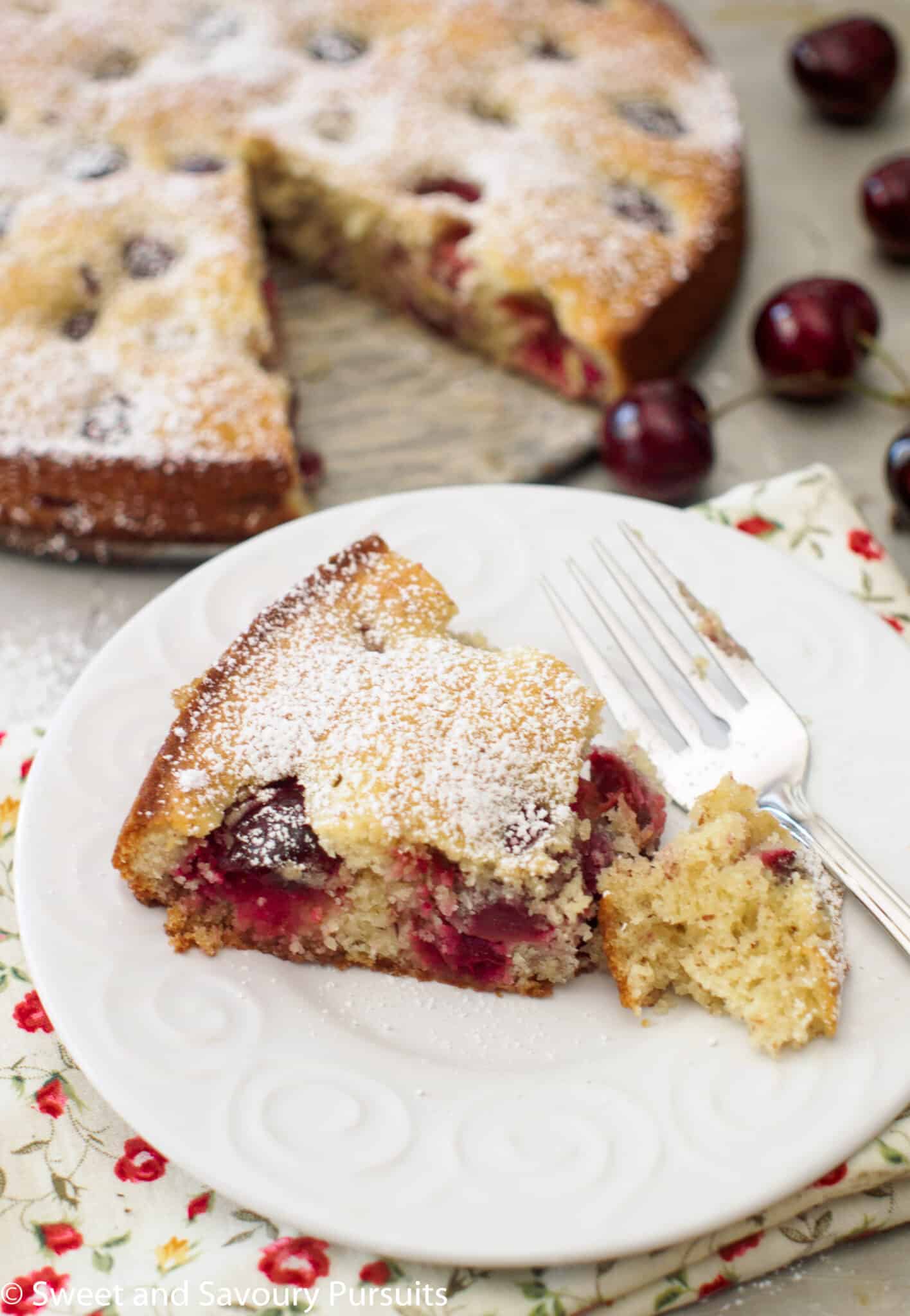 Slice of Cherry Almond Cake with a dusting of powdered sugar on white dish.