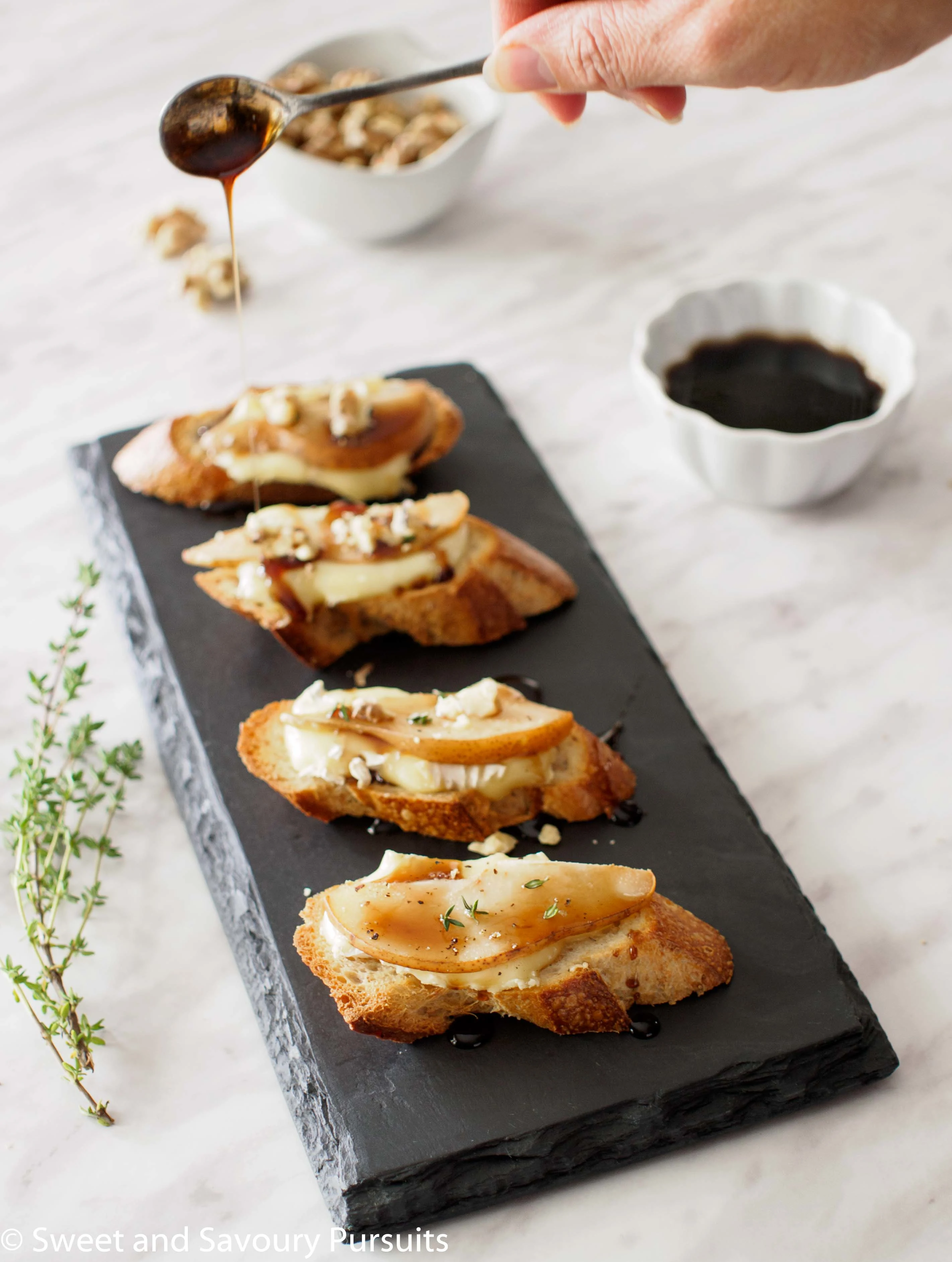 Pear and Brie Crostini topped with balsamic syrup and crumbled walnuts.