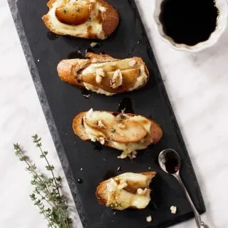 Pear and Brie Crostini drizzled with a honey and balsamic syrup and topped with crumbled walnuts and a sprinkle of fresh thyme leaves.