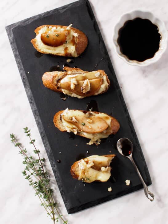 Pear and Brie Crostini drizzled with a honey and balsamic syrup and topped with crumbled walnuts and a sprinkle of fresh thyme leaves.