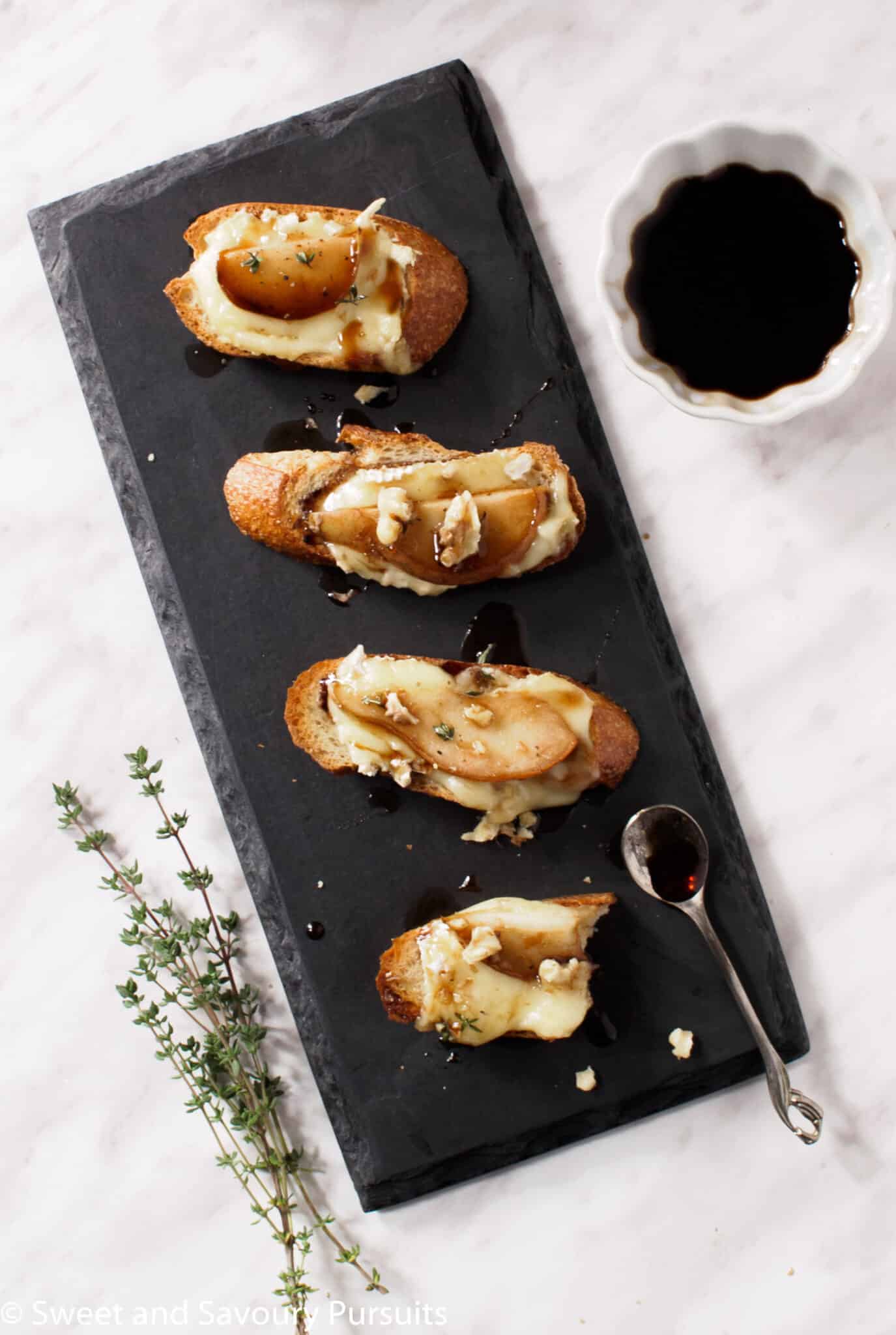 Pear and Brie Crostini drizzled with a honey and balsamic syrup and topped with crumbled walnuts and a sprinkle of fresh thyme leaves.