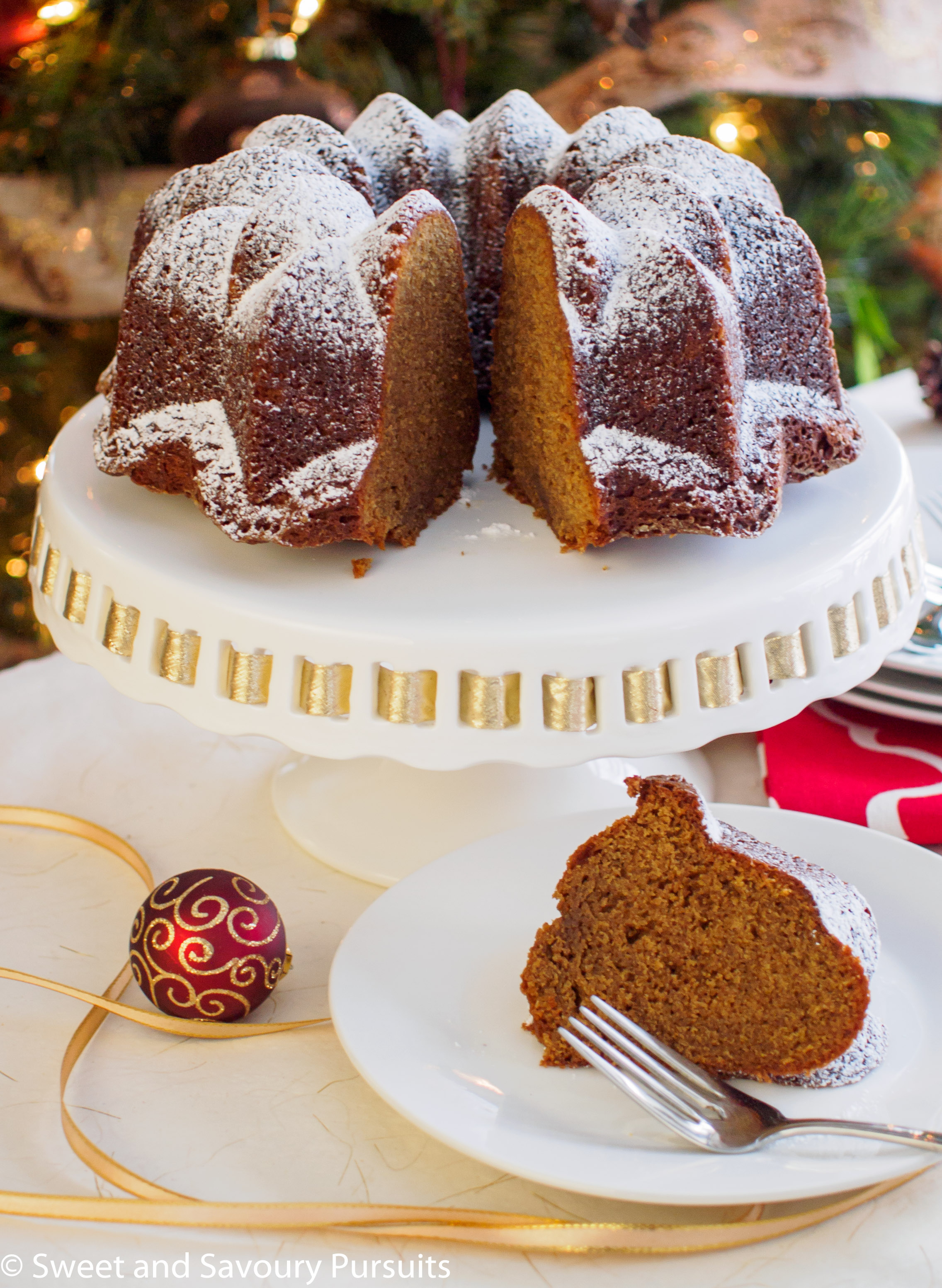 Gingerbread bundt cake on platter with cut slice on plate.