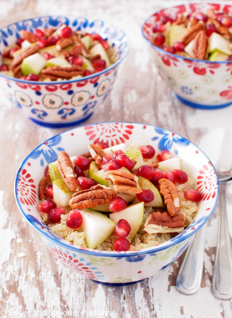 Three quinoa breakfast bowls topped with pears, pomegranate and pecans.
