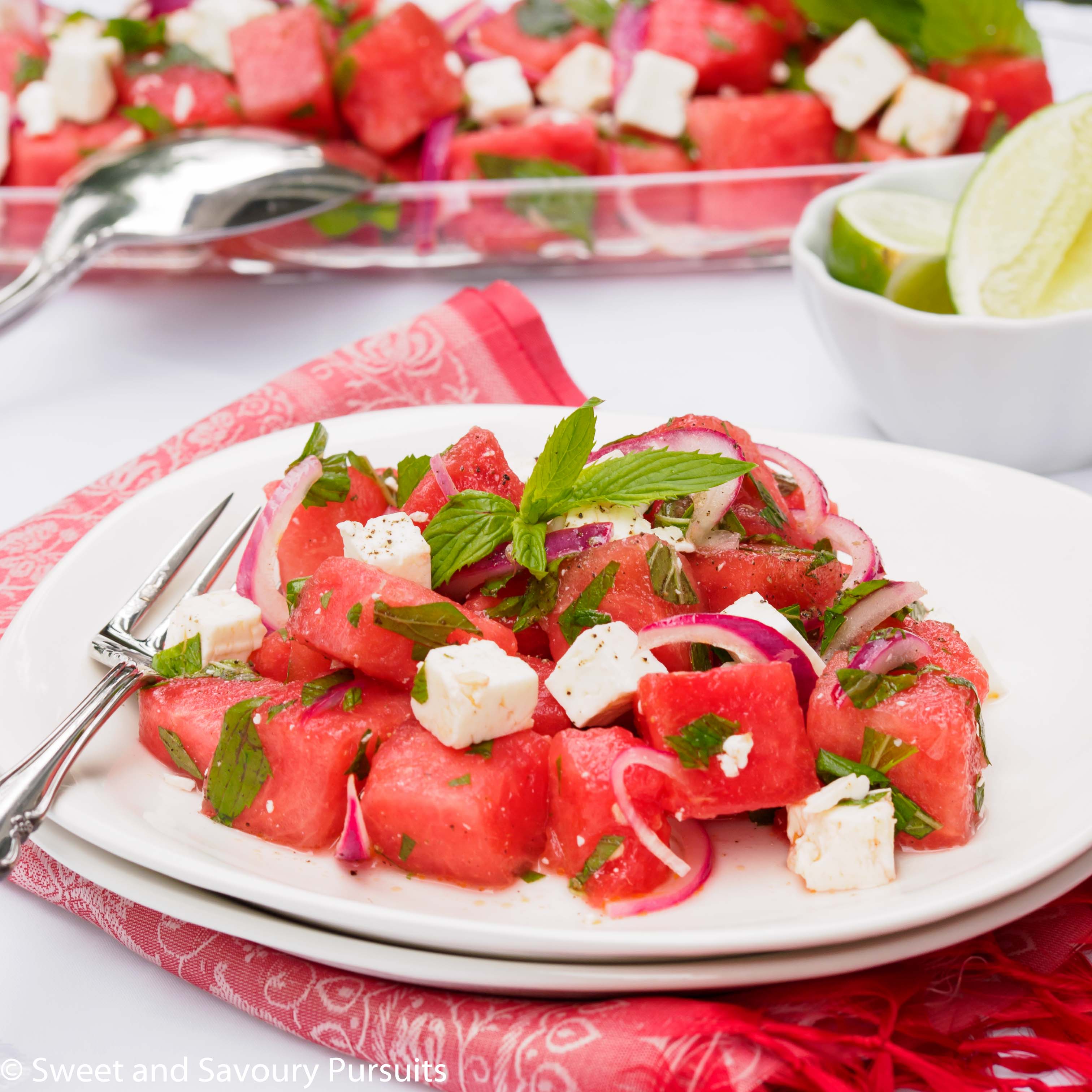 Salad made with cubed watermelon and feta cheese topped with fresh mint leaves and served on white dish.