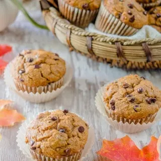 Three Pumpkin Chocolate Chip Muffins on a board with a basket of muffins in the background.