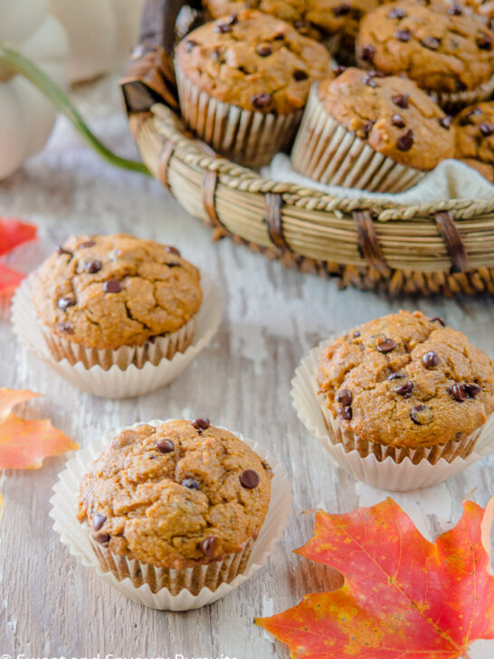 Three Pumpkin Chocolate Chip Muffins on a board with a basket of muffins in the background.