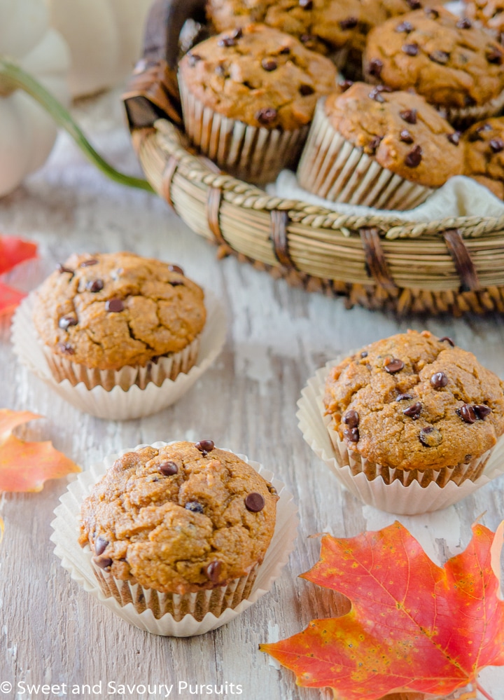 Three Pumpkin Chocolate Chip Muffins on a board with a basket of muffins in the background.