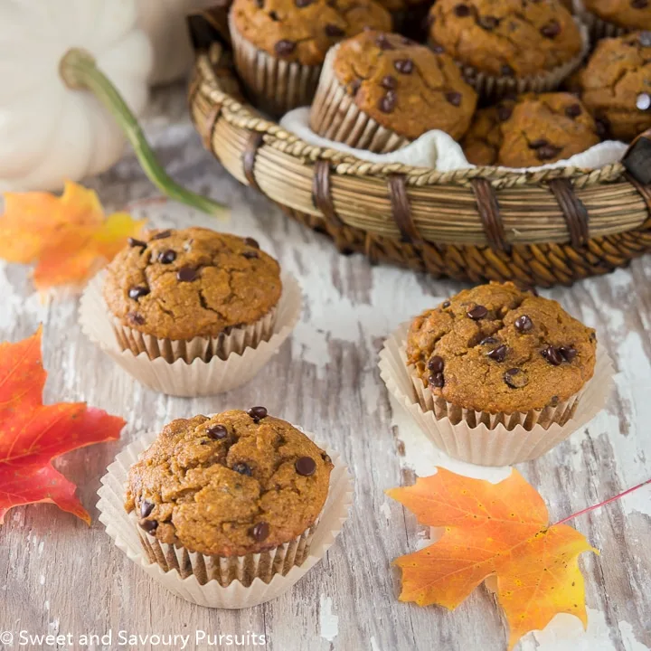 Whole Wheat Pumpkin Chocolate Chip Muffins on board with basket of muffins in the background.