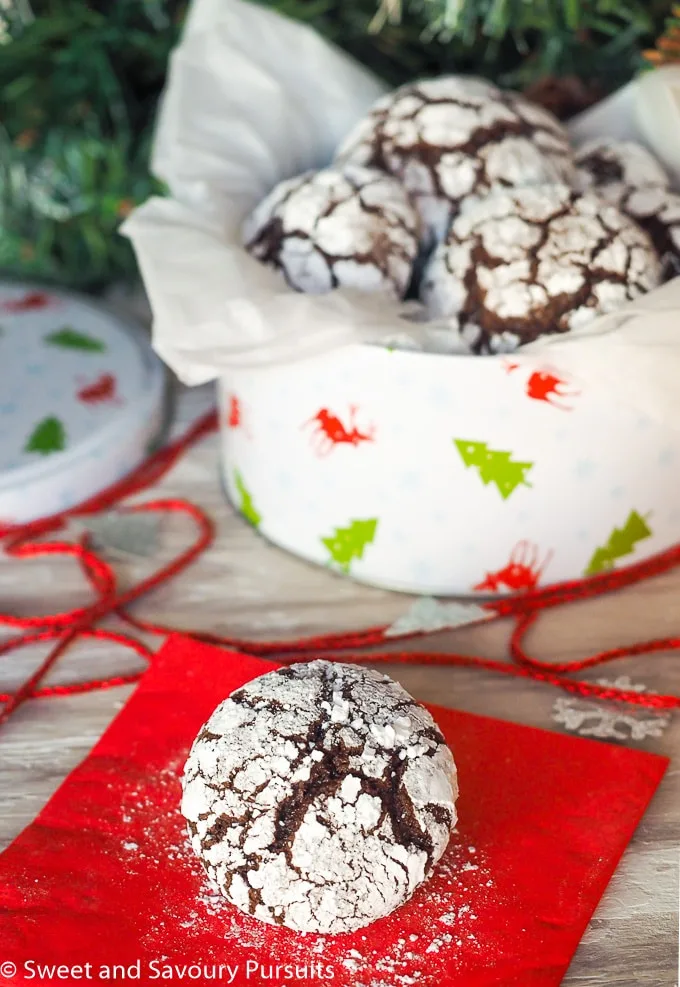 Tin of Chocolate Crinkle Cookies with cookie on napkin.