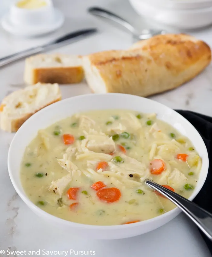 A bowl of creamy chicken noodle soup served with bread.