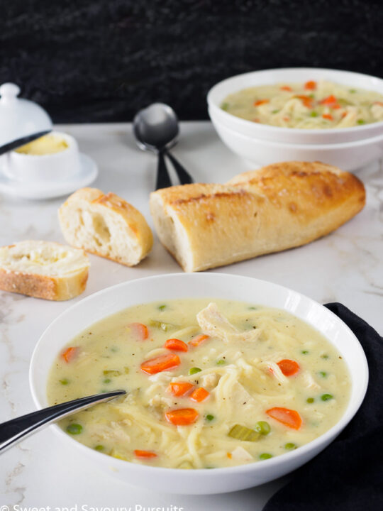 Bowl of Creamy Chicken Noodle and Vegetable Soup served with sliced bread.