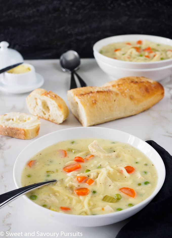 Bowl of Creamy Chicken Noodle and Vegetable Soup served with sliced bread.