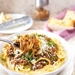 Close-up of spaghetti and meat sauce twirled around a fork. Garlic bread in background.