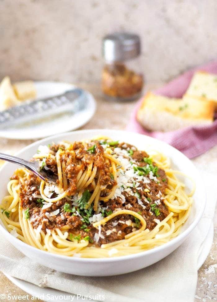 Close-up of spaghetti and meat sauce twirled around a fork. Garlic bread in background.