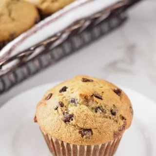 Banana chocolate chip muffin on dish with basket of muffins in background.