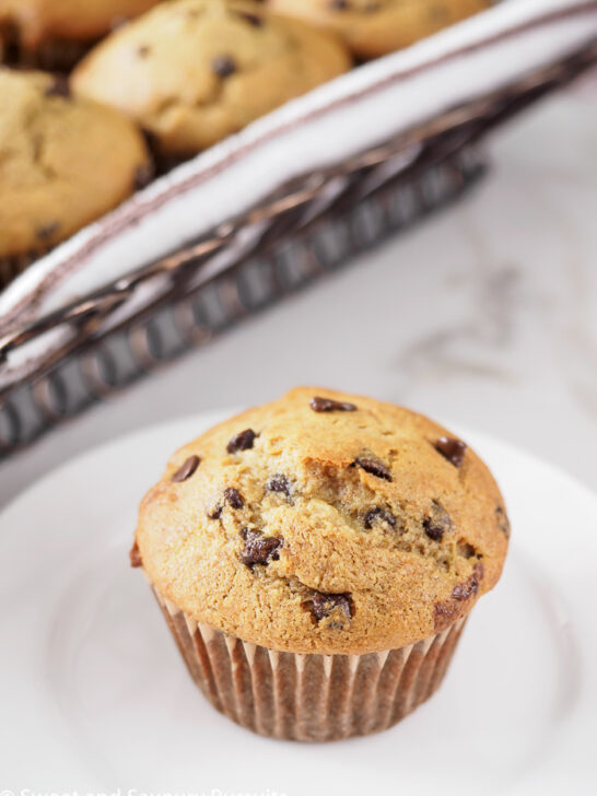 Banana chocolate chip muffin on dish with basket of muffins in background.