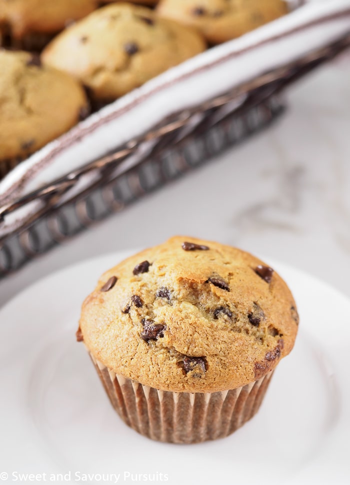 Banana chocolate chip muffin on dish with basket of muffins in background.