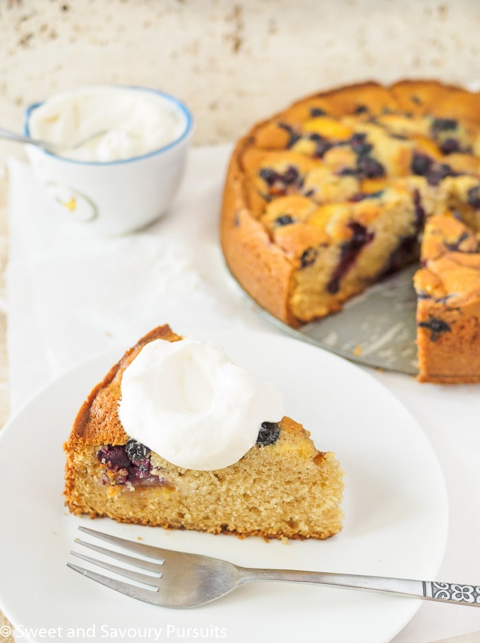 Peach and Blueberry cake on a white plate with a dollop of freshly whipped cream.