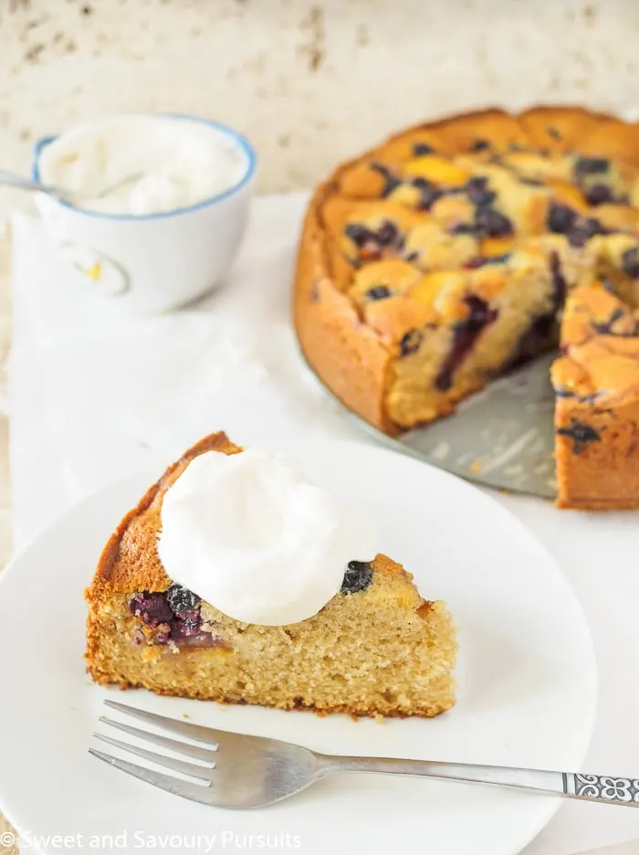 Peach and Blueberry cake on a white plate with a dollop of freshly whipped cream.