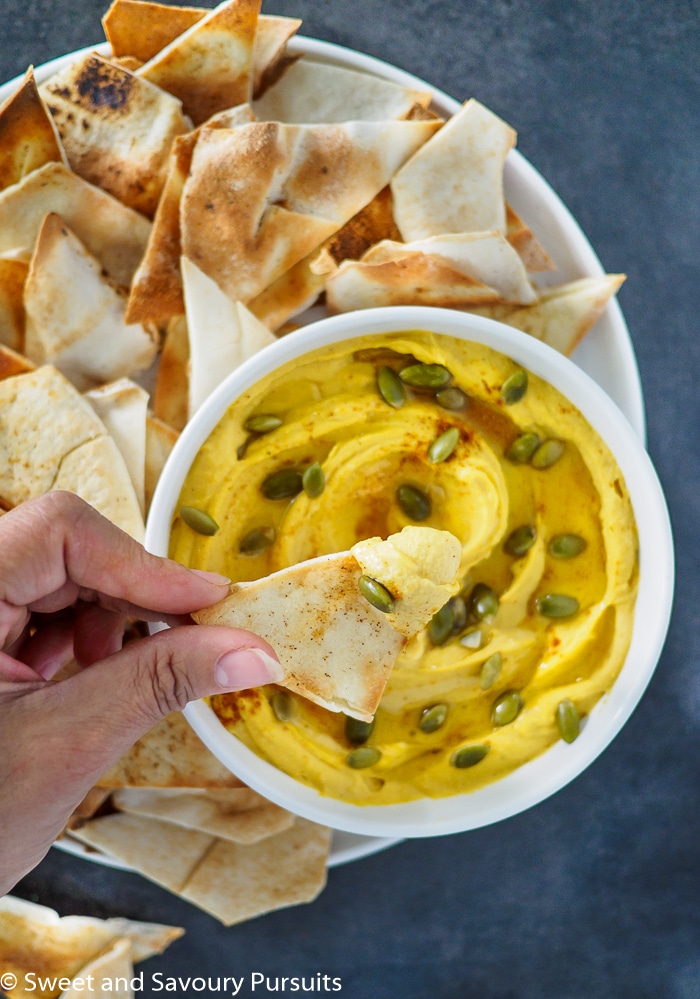 A close up of a chip with squash and white bean dip on it.