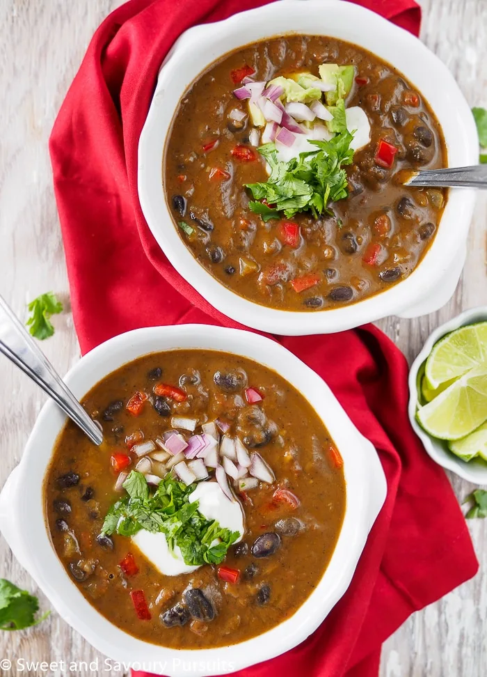 Two bowls of Black Bean Soup with topped with cilantro, onion and sour cream.