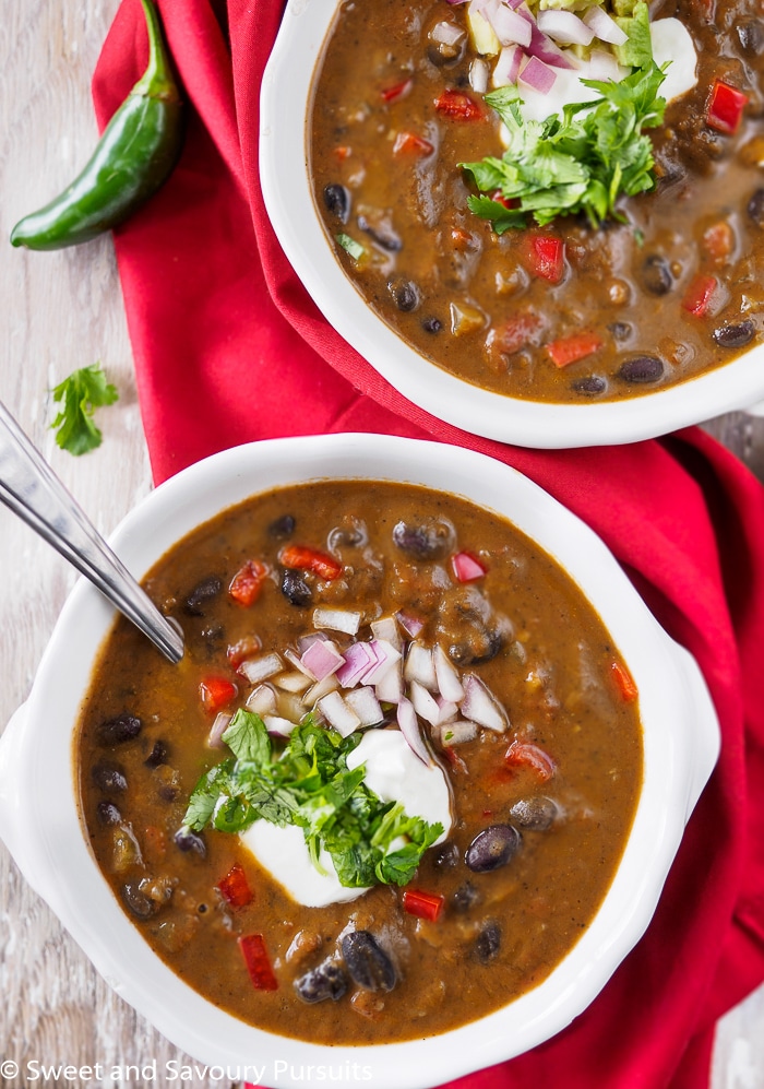 Two bowls of black bean soup topped with sour cream and chopped cilantro.