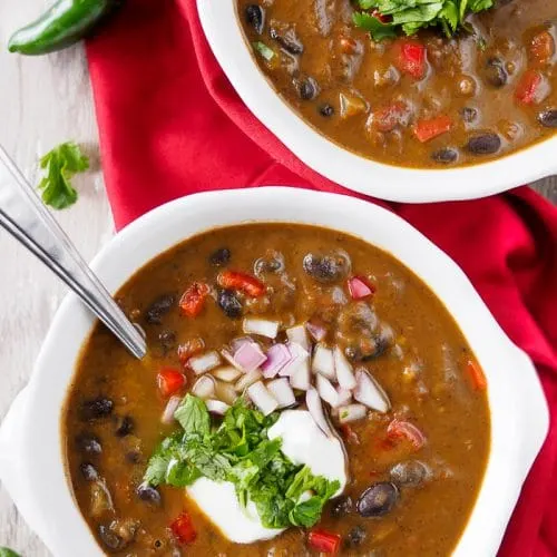 Bowls of Black Bean Soup topped with chopped cilantro, onion and sour cream.