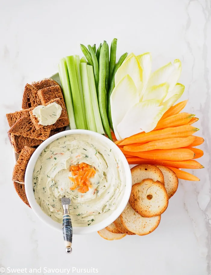 Top view of a bowl of Smoked Salmon and Cream Cheese Dip served with vegetables, pumpernickel bread and crackers.