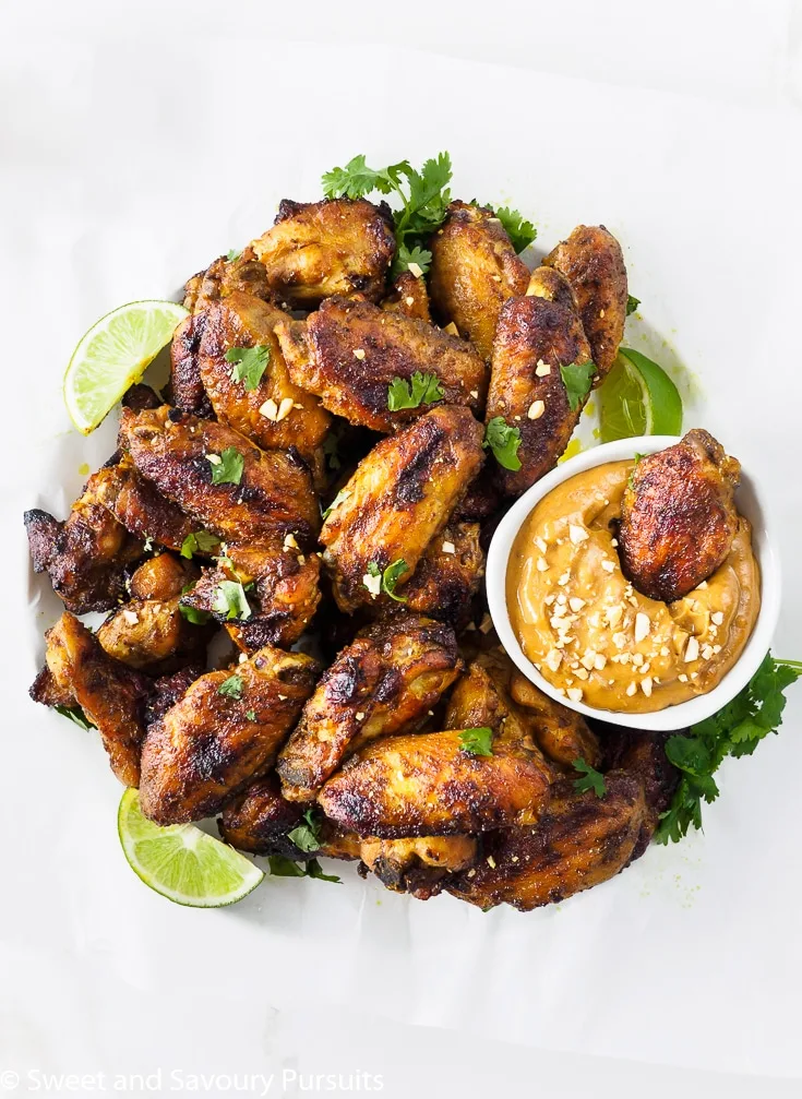 Platter of Thai Chicken Wings with a chicken wing dipped in a bowl of peanut sauce.