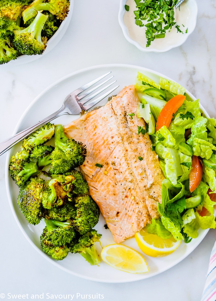 Top view of a fillet of rainbow trout fish with a side of roasted broccoli and of salad.