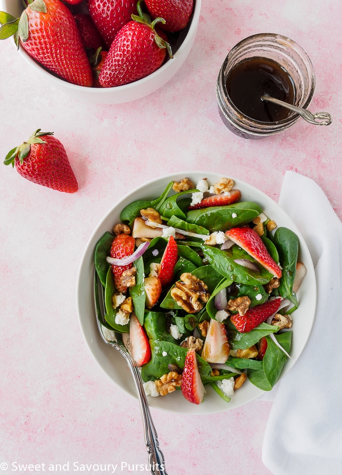 Bowl of a strawberry spinach salad dressed with a balsamic vinaigrette.