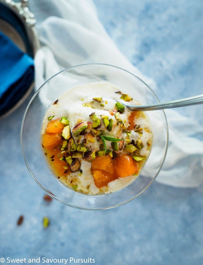 Bowl of vanilla ice cream topped with peach sauce and chopped pistachios.