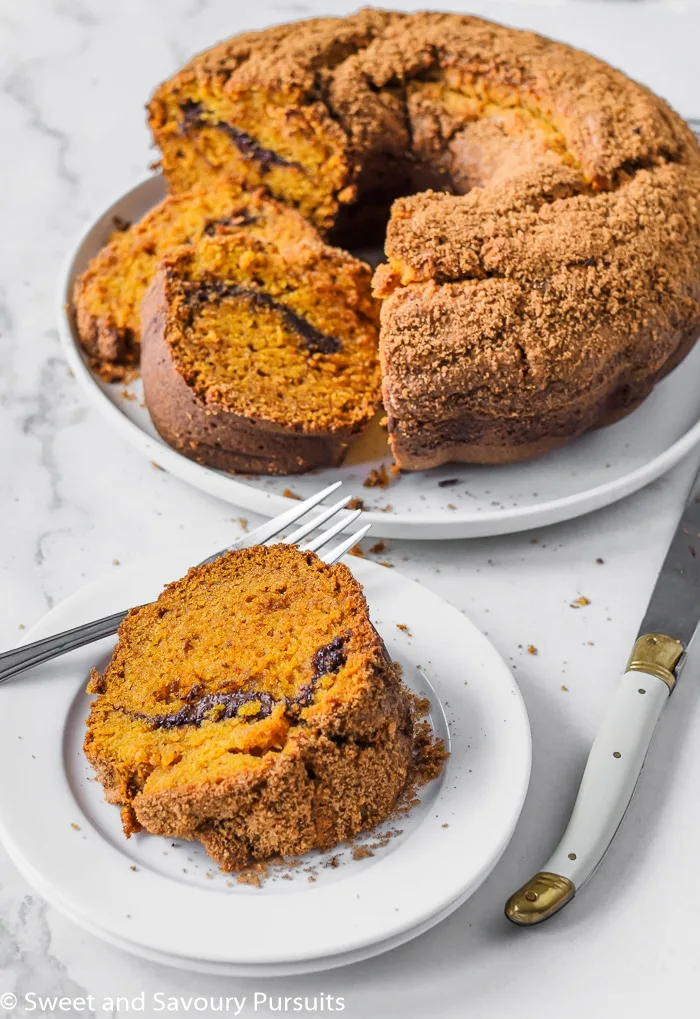 A slice of pumpkin bundt cake on a small dish with the rest of the cake in the background. 