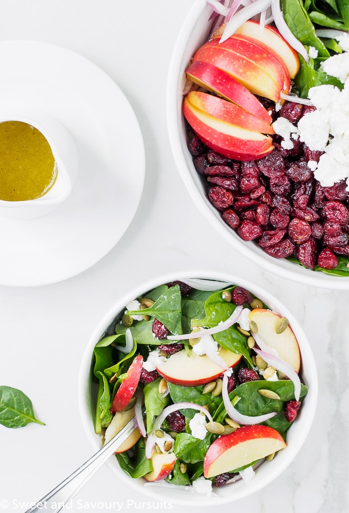 Bowl of Spinach Apple Cranberry Salad with Pumpkin Seeds served with Apple Cider Vinaigrette on the side.