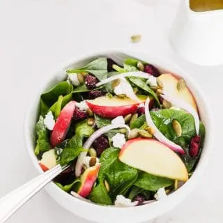 Small bowl of spinach salad with apple, dried cranberries and pumpkin seeds.
