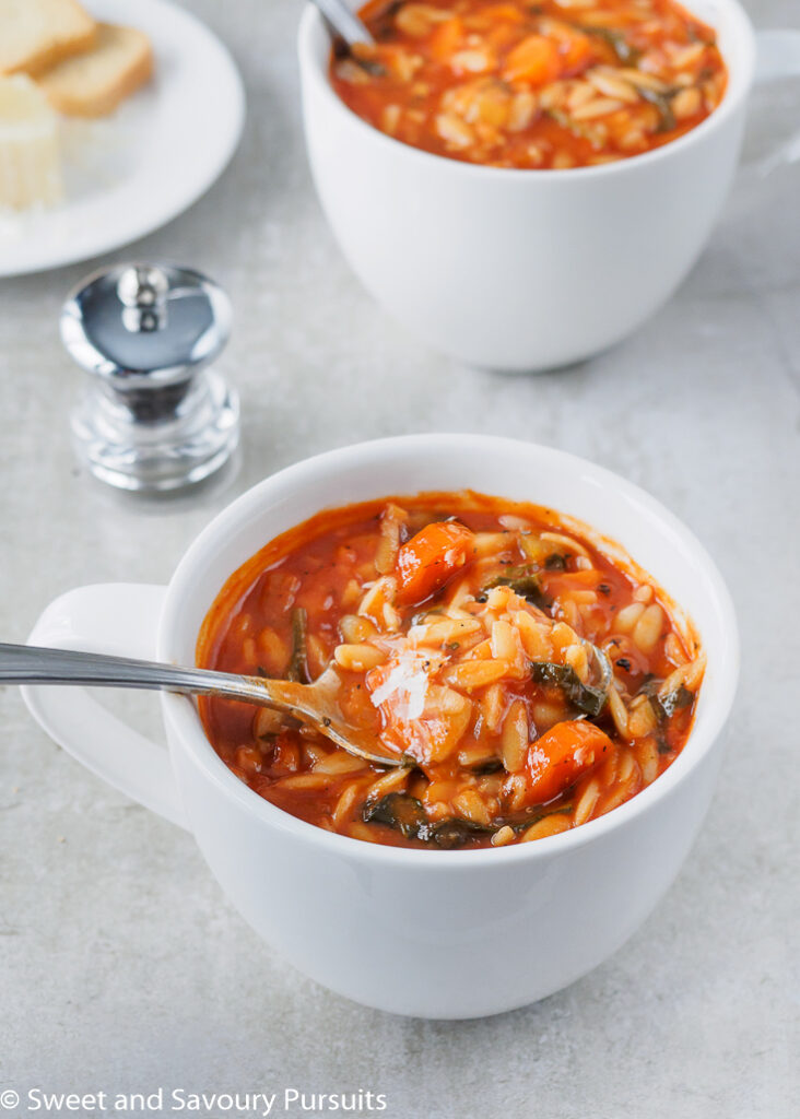 Tomato Orzo Soup with freshly grated Parmesan cheese in large white mug.