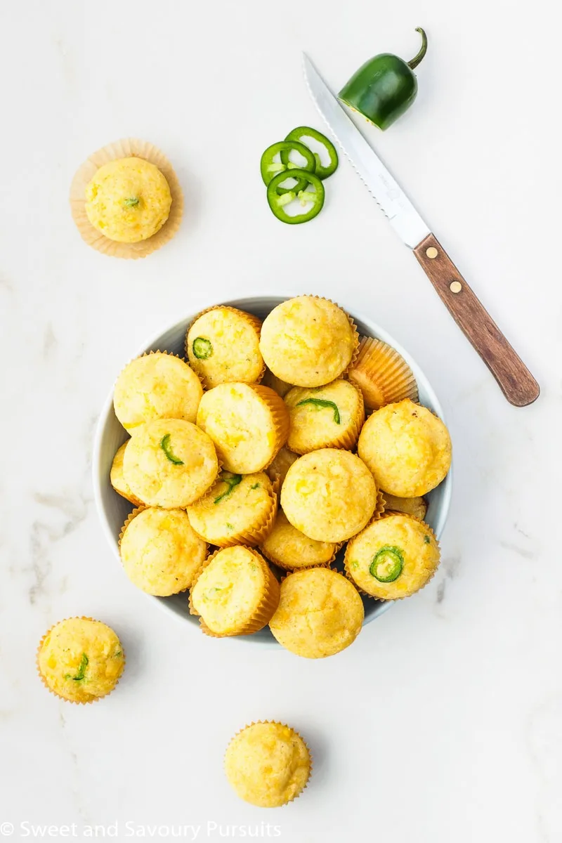 Freshly baked Mini Cornbread Muffins with corn kernels and jalapeño in bowl.