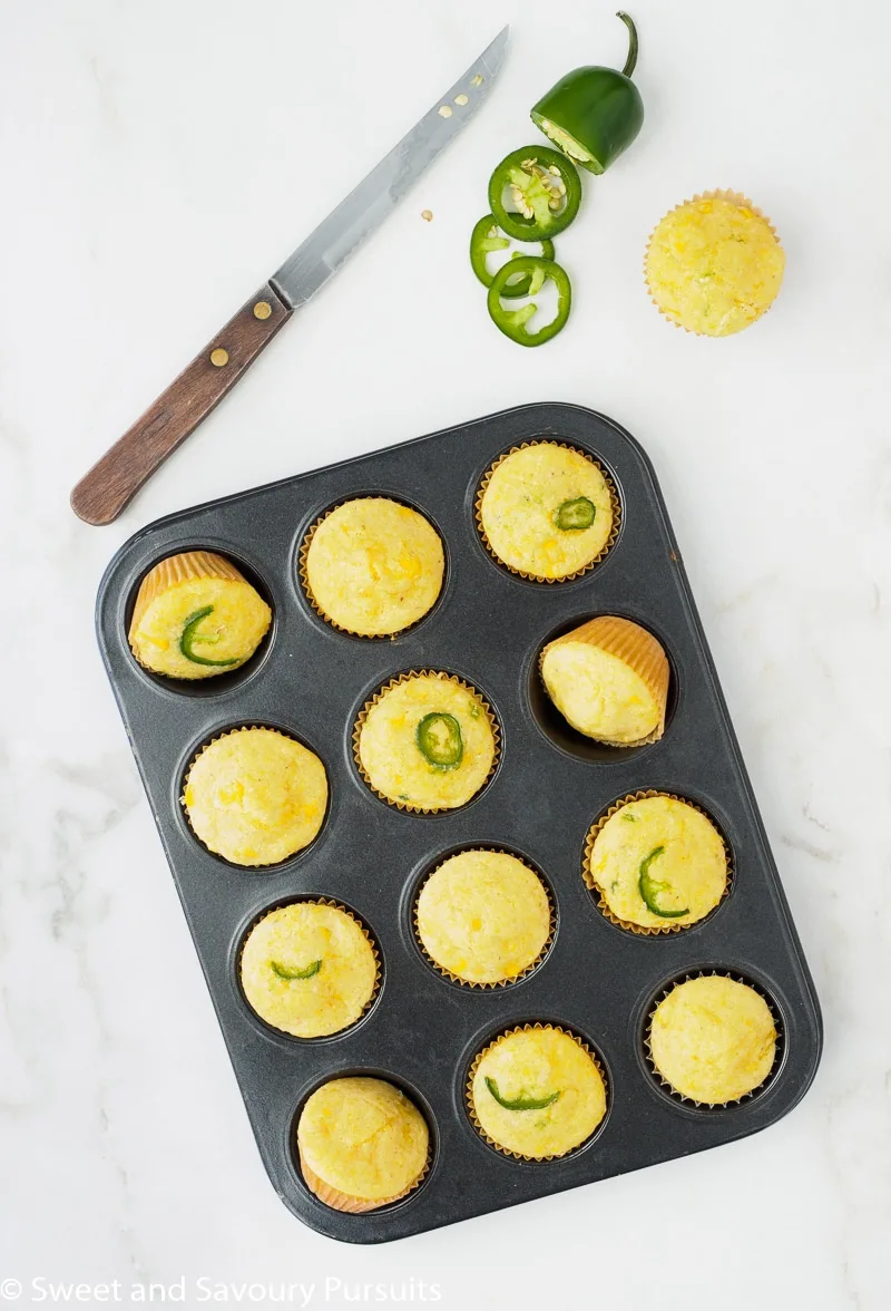 Freshly baked Mini Cornbread Muffins with corn kernels and jalapeño still in muffin tin.