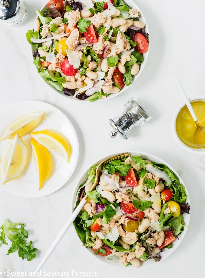 Two bowls of white bean and tuna Salad with lemon and olive oil dressing served on the side.