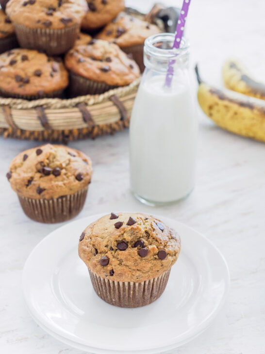 A basket of Banana Oatmeal Chocolate Chip Muffins and one muffin on small dish served with milk.
