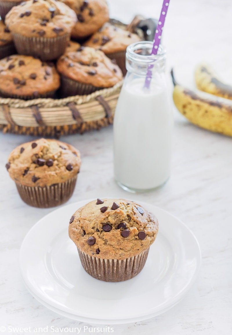 A basket of Banana Oatmeal Chocolate Chip Muffins with one muffin on small dish served with milk.