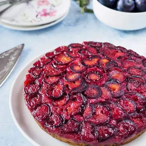 Plum Upside Down Cake on white dish with fresh plums in background.