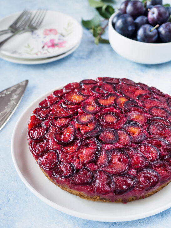 Plum Upside Down Cake on white dish with fresh plums in background.